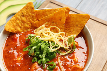 Bowl with delicious chili turkey and nachos on wooden board, closeup