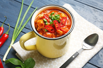 Enamel mug with delicious chili turkey on table