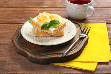 Plate with delicious lemon pie bars and cup of tea on table
