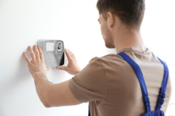Young electrician installing security alarm on wall - obrazy, fototapety, plakaty