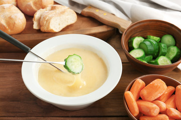 Cheese fondue with cucumber on table