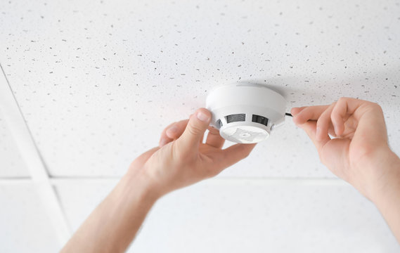 Electrician installing smoke detector on ceiling, closeup