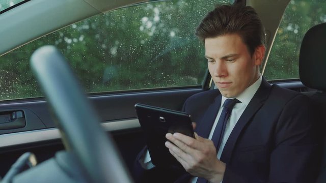 Thoughtful handsome businessman using tablet in the car 4K