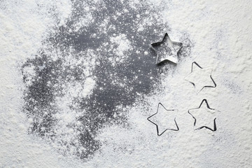Cookie cutter in shape of star and flour on dark background