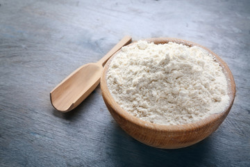 Bowl with flour and scoop on wooden background