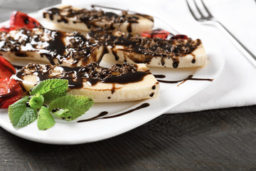 Plate with tasty bananas and chocolate sauce on wooden table, closeup
