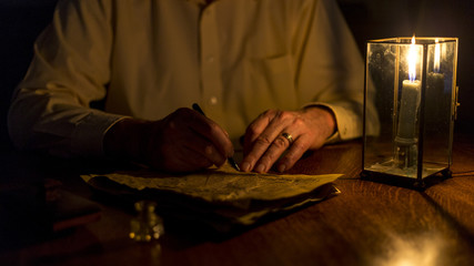 A grandfather writes a letter under candlelight on old, wrinkled paper. 