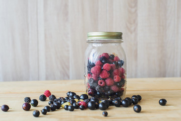 Red, white, black currant, red and black raspberries, white strawberries in glass jar and sprinkle on wooden table as  canned food