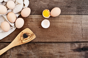 Farm fresh organic brown chicken eggs from free range chickens with an old olive wood antique spatula over a rustic wooden background. One egg cracked open showing yolk.