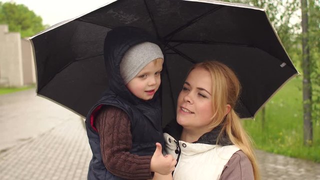Portrait of mom with the son in a rainy day under a black umbrella in the Park.