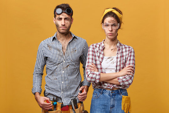 Studio portrait of confident serious young European family of mechanics or electricians standing close to each other against blank wall background with copy space for your advertising content