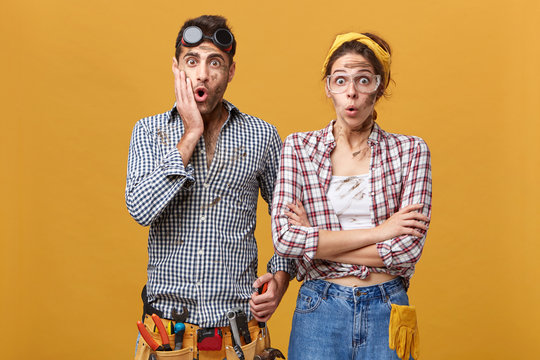 Human emotions, feelings, attitude and reaction. Emotional handyman equipped with working instruments touching cheek in shock, his astonished female colleague standing next to him with eyes popped out