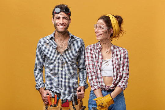 Two cheeful craftsmen enoying results of their work, standing next to each other with dirty but happy faces. Male and female electricians having a break while doing renovations in residential house