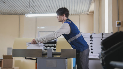 The printing house employee is working on printing at the machine