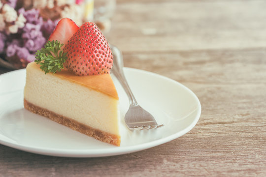 Homemade New York cheesecake on white plate decorated by strawberry and parsley. Moist and smooth classic style baked cheesecake. Copy space background of delicious strawberry New York cheesecake.