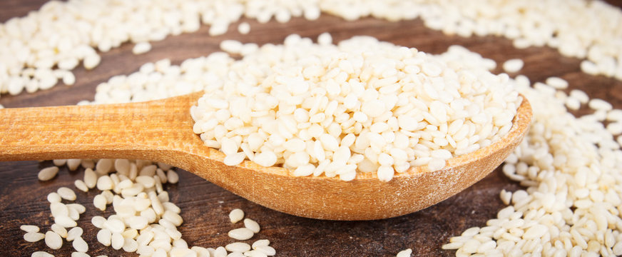 Sesame seeds with spoon on rustic board, healthy nutrition concept