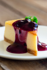 Homemade blueberry cheesecake on white plate decorated with parsley and blueberry sauce. Moist and smooth classic baked cheesecake. Copy space background of delicious blueberry New York cheesecake.