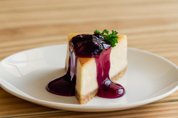 Homemade blueberry cheesecake on white plate decorated with parsley and blueberry sauce. Moist and smooth classic baked cheesecake. Copy space background of delicious blueberry New York cheesecake.
