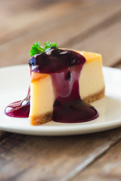 Homemade blueberry cheesecake on white plate decorated with parsley and blueberry sauce. Moist and smooth classic baked cheesecake. Copy space background of delicious blueberry New York cheesecake.
