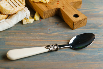 Tablespoon lying on a wooden table. Kitchen board with toasted loaves on the background of composition.