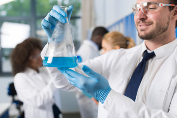 Male Scientist Working With Flask In Laboratory Making Research Over Mix Race Team Of Lab Workers Busy with Experiments