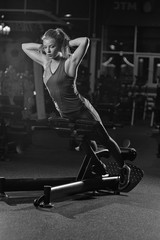 Fototapeta na wymiar Woman doing strength exercises for abdominal muscles at indoor sport gym. Girl doing yoga stretches after running. Fitness model in dark sport club. Black and white.