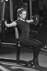 Fototapeta na wymiar Woman at the sport gym doing arms exercises on a machine. Black and white sport club.