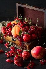 Casket for decorations with fruits and berries on dark wooden background. Selective focus. Low key
