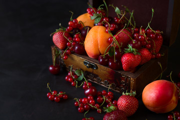Casket for decorations with fruits and berries on dark wooden background. Selective focus. Low key