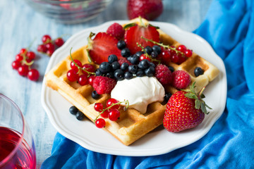 Healthy breakfast: Belgian waffles with sour cream, strawberry, raspberry, blueberry, cherry and red currant on blue wooden table. Selective focus