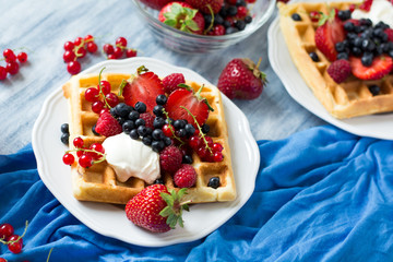 Healthy breakfast: Belgian waffles with sour cream, strawberry, raspberry, blueberry, cherry and red currant on blue wooden table. Selective focus