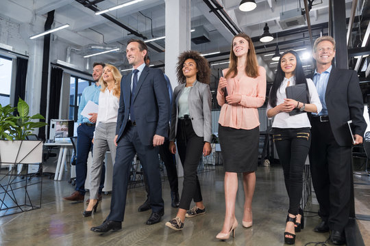 Full Length Business People Team Walking In Modern Office, Confident Businessmen And Businesswomen In Suits Diverse With Mature Leader In Foreground