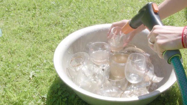 Female hands with garden hose washing wine glasses placed in basin with water