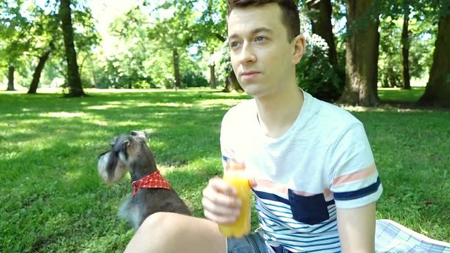 Boy relaxing with his dog in the park and drinking orange juice, steadycam shot
