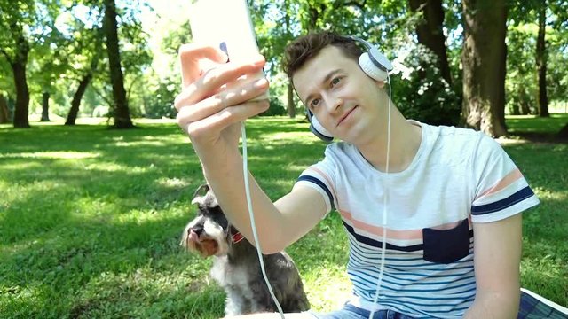 Boy relaxing with his dog in the park and doing selfies on smartphone, steadycam shot
