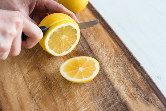 Close up high angle view of middle aged woman's hand slicing lemon on wooden chopping board (selective focus)