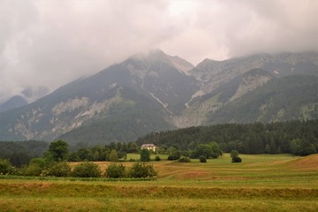 Felder mit Wald und bewölkter Berglandschaft