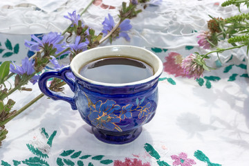Blue cup of coffee tea chicory drink with chicory flower,  hot beverage on embroidered fabric background