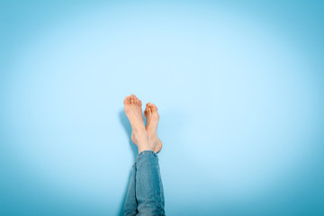Plakat Female legs foot on foot on blue wall, resting, holiday