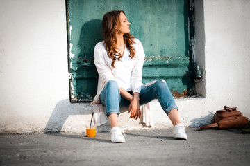 Enjoy woman beautiful sitting on street near green wooden door, healthy drink, cup orange juice, outdoor on street lifestyle, warmly