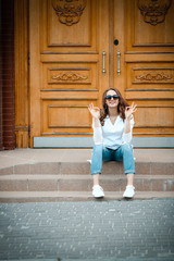 Smiling woman in sunglasses sitting on stone steps in city urban, walking on town, positive, outdoor, wooden door background