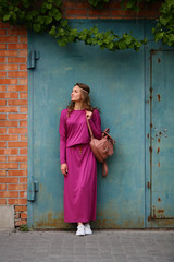 Beautiful young modern woman standing front, full length,looking away, in casual dress clothing, on urban background, purple, bag, outdoor, city, street lifestyle, bag