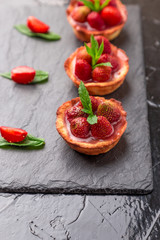 Homemade strawberries tarts on slate plate, black background