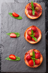 Homemade strawberries tarts on slate plate, black background. Top view.