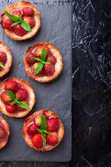 Homemade strawberries tarts on slate plate, black background. Top view.