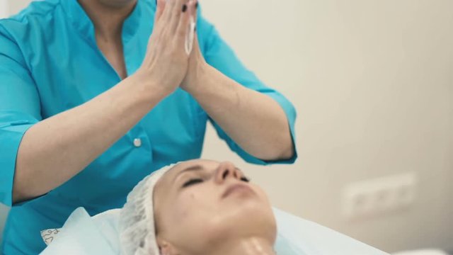 The employee of the spa salon applies an ennobling cream on the face of a young attractive girl close up