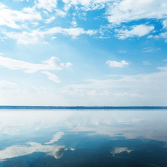 deep blue sky with clouds over river and reflection of it