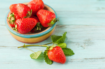 Ripe strawberries in a cup on a wooden, turquoise background.