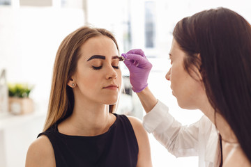 Portrait of a young woman while painting her eyebrows in the salon. The process of correction and coloring of eyebrows