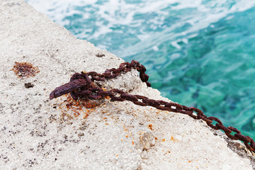 Old hook with rusted chain mounted in concrete sea pier. Mooring equipment for fishing boats and small ships.